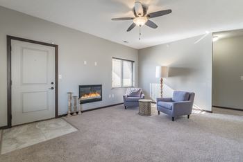 Carpeted living room with electric fireplace and ceiling fan at The Villas at Wilderness Ridge in South Lincoln, Nebraska